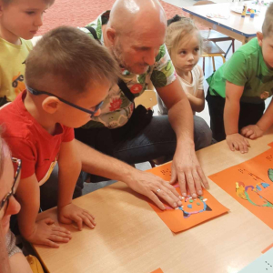 Osoba niewidoma za pomocą zmysłu dotyku odgaduje obrazki przygotowane przez dzieci. 