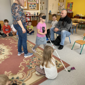 Dziecko za pomocą laski dla osób niewidomych oraz własnego słuchu szuka breloczka wydającego dźwięk.