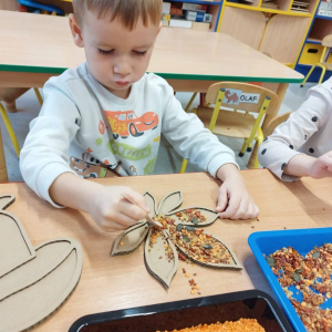 Dzieci rozwijają sprawność manualną przy pomocy wysypywanek w jesiennych kształtach, wypełnianych kaszą, kukurydzą, grochem i soczewicą.